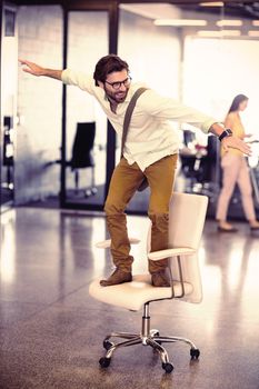 Male business executive standing on chair in office