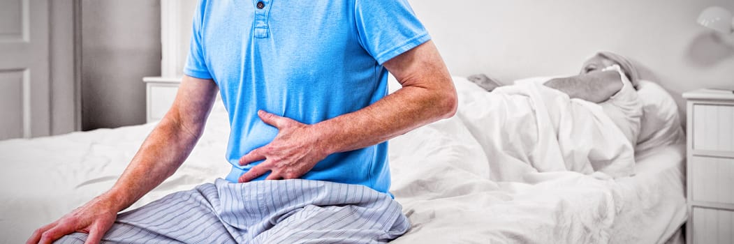 Senior man having stomach pain while sitting on bed at home