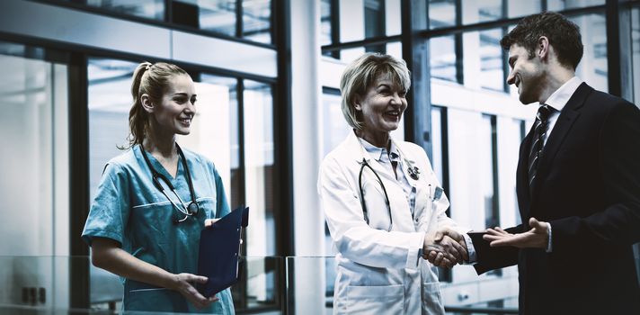 Female doctor shaking hands with businessman in hospital