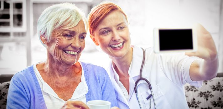 Smiling doctor and patient looking at phone while having tea at home