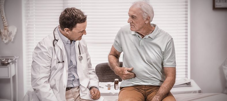 Senior man showing stomach ache pain to doctor in clinic