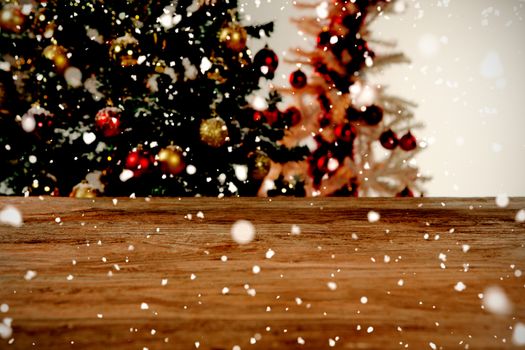 Snow falling against wooden table in christmas tree in background