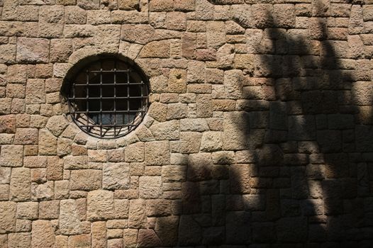 Stone wall with circular church window with wooden shadow.