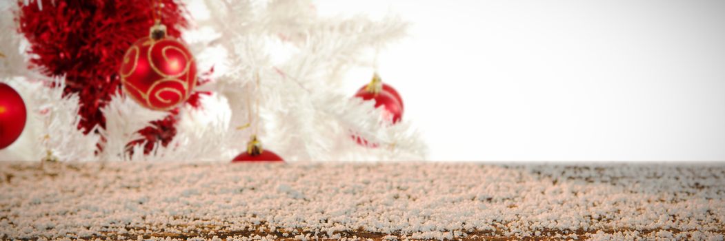 Wooden table covered with snow against red and white christmas decorations