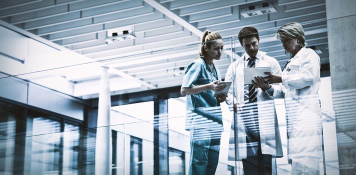 Medical team discussing over digital tablet in corridor at hospital