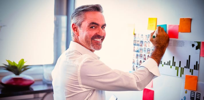 Portrait of happy mature businessman making strategies on whiteboard in creative office