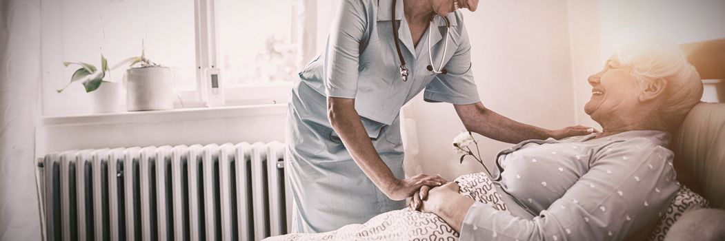 Nurse interacting with senior woman on bed at bedroom