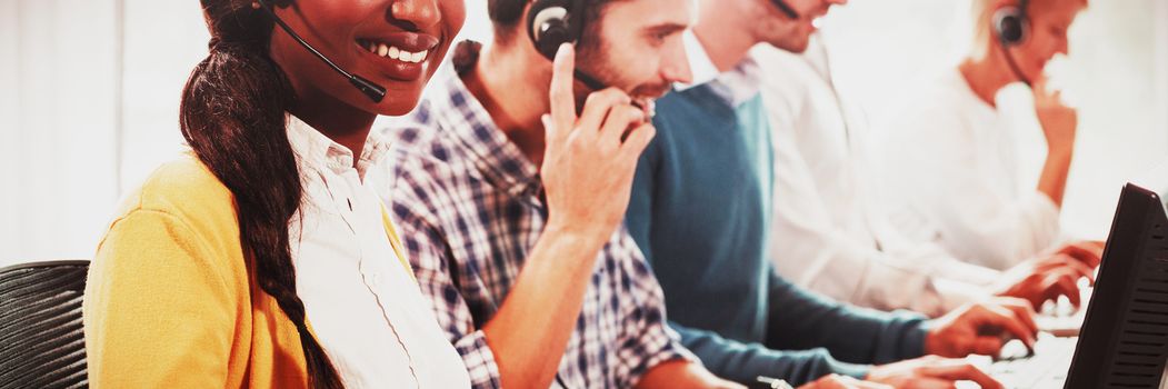 Team working on computer with headset while a colleague smiling at camera in the office