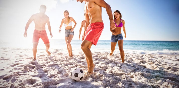 Cheerful friends playing football at beach