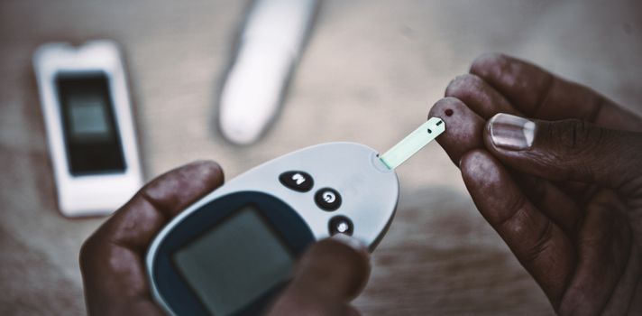 Cropped hands of person using glucometer to check blood sugar