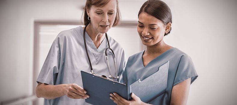 Nurse and doctor discussing over clipboard in hospital corridor