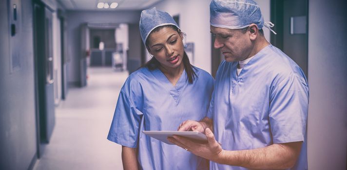 Surgeons discussing over digital tablet in hospital corridor