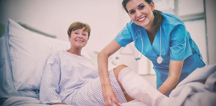 Portrait of smiling nurse bandaging leg of patient in hospital