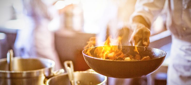 Chef tossing stir fry over large flame in commercial kitchen