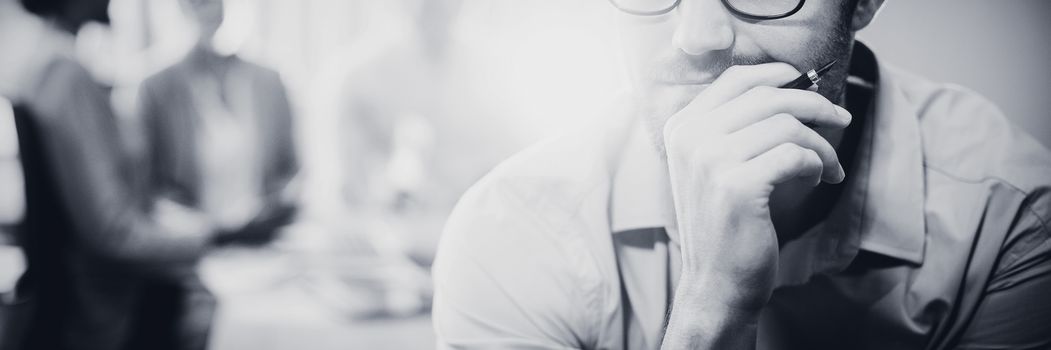 Thoughtful man with hand on chin while coworker interacting in the background in the office