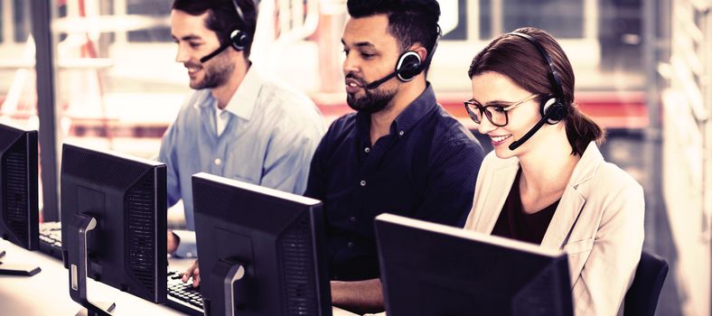 Smiling business executives with headsets using computers at desk in office