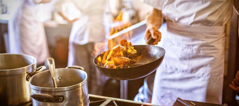 Midsection of chef tossing stir fry over large flame in commercial kitchen