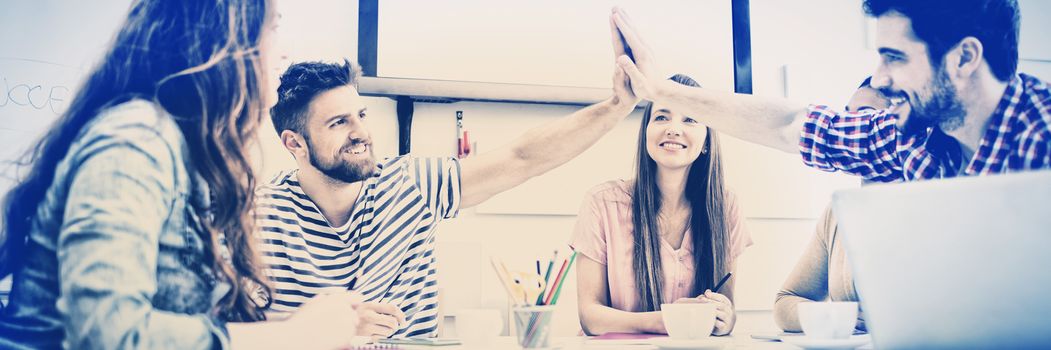 Male colleagues giving high-five while female executives in meeting at creative office