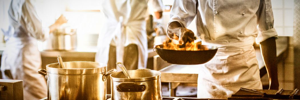 Chef tossing stir fry over large flame in commercial kitchen