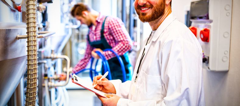 Portrait of maintenance workers examining brewery machine at brewery factory