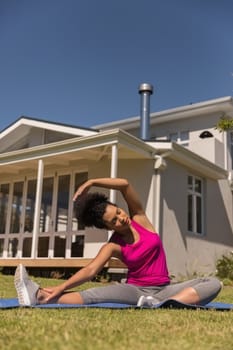 Front view of a beautiful young fit mixed-race woman performing stretch exercise in the backyard of home