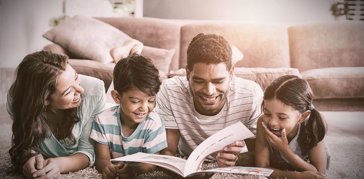 Parents and children lying on rug and reading book in living room at home