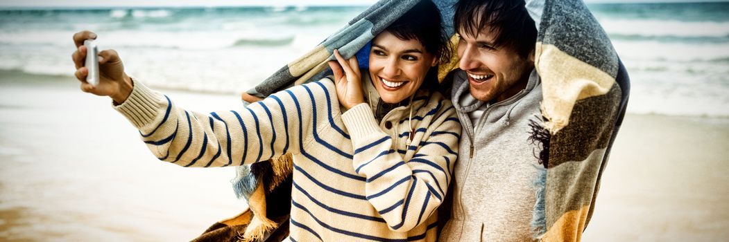 Happy young couple taking selfie at beach during winter