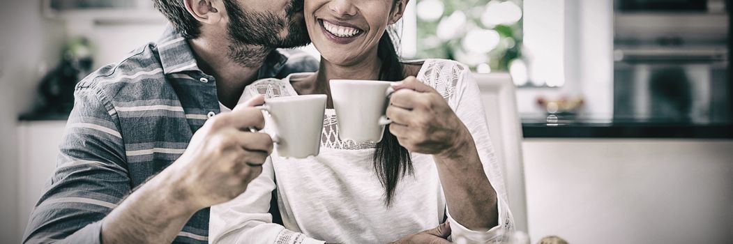 Man kissing on woman cheeks while having breakfast at home