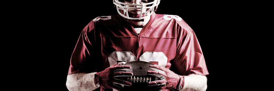 American football player holding rugby ball against black background