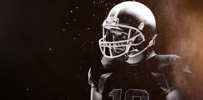 Digitally generated image of powder against american football player standing with rugby helmet