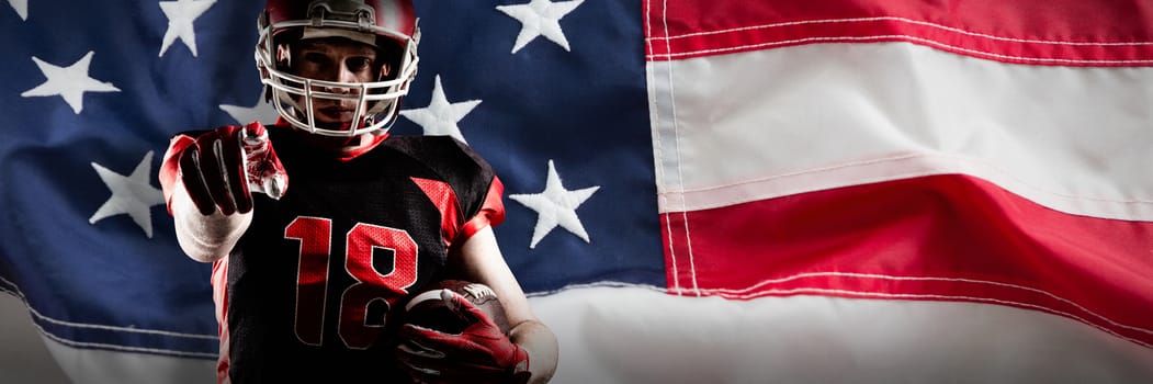 American football player in helmet holding rugby ball and pointing against full frame of american flag