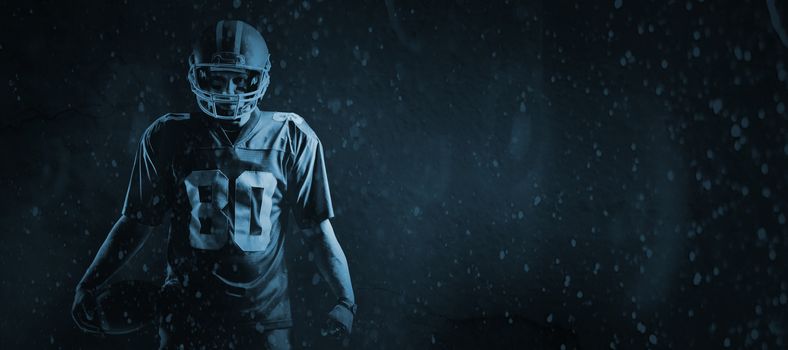 American football player standing with rugby ball against old weathered wall