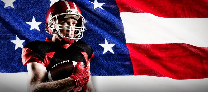 American football player in helmet standing with rugby ball against close-up of an american flag