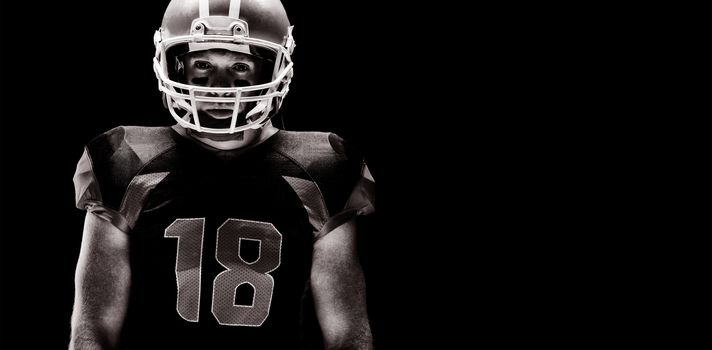 American football player standing with rugby helmet against black background