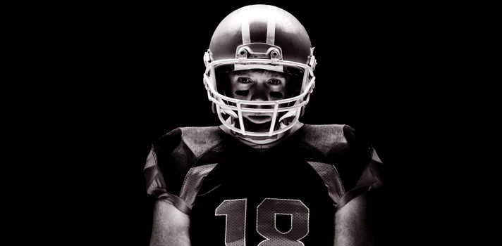American football player standing with rugby helmet against black background