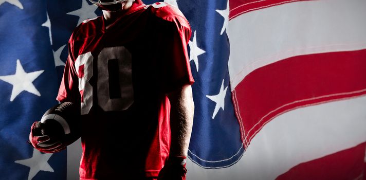 American football player in helmet holding rugby ball against close-up of an american flag