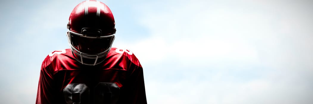 American football player standing in rugby helmet against blue sky with clouds 