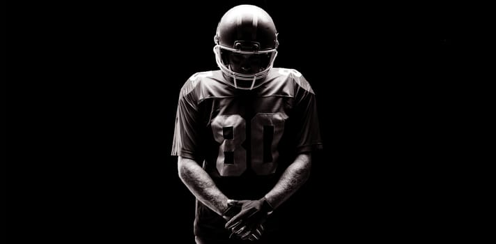 American football player standing with rugby helmat against black background
