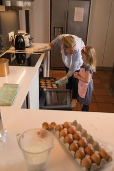 Side view of loving mother with her daughter removing cookies from oven in kitchen at home