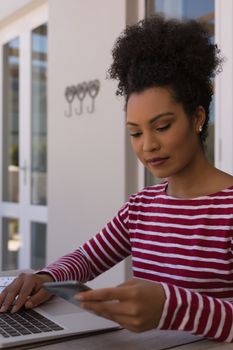 Side view of a beautiful African American woman using mobile phone while working on her laptop at home