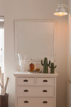 Front view of a modern mirror fixed above a cabinet supporting a vases, bottles of alcohol and false cactus at home