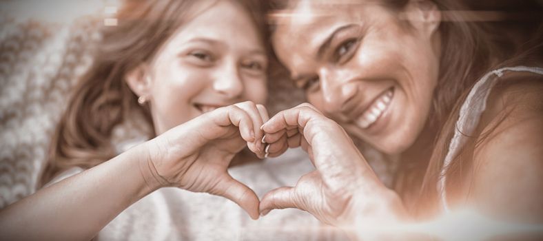 Mother and daughter making heart shape with hands while lying on bed at home