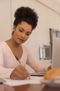 Front view of African American beautiful woman filling a form while using laptop at home