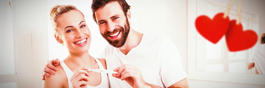 Hearts hanging on a line against portrait of happy couple checking pregnancy test