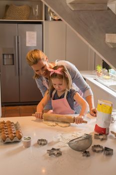 Front view of happy mother with her daughter preparing cookie dough in kitchen at home