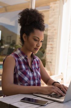 Side view of a beautiful  African American woman using her laptop on a table of the terrace at home