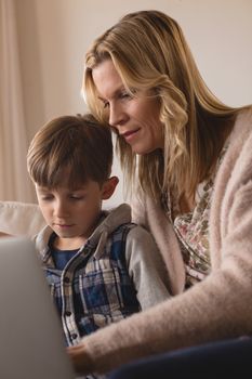 Front view of concentrated mother helping her son use laptop in living room at home