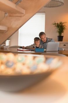 Distant front view of caring father helping his son with his homework while using laptop at home