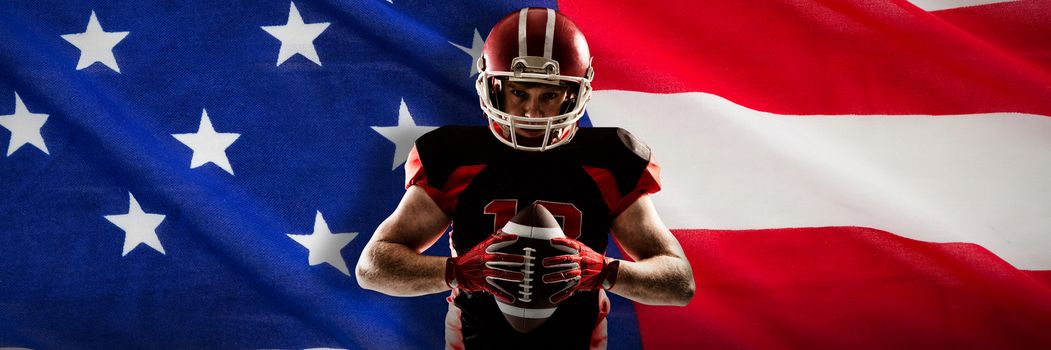 American football player standing with helmet and ball against close-up of an american flag