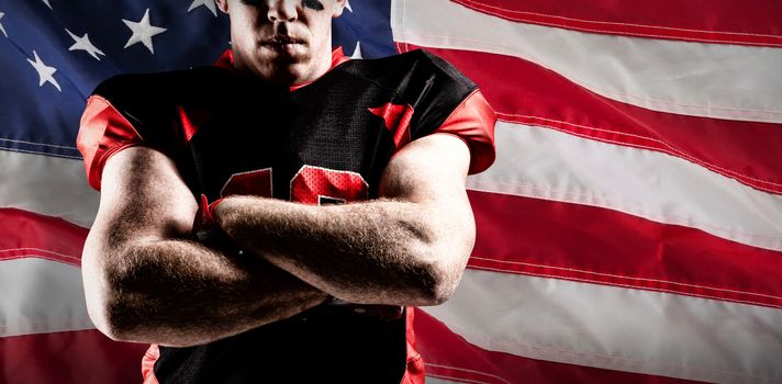 American football player standing with arms crossed against close-up of an american flag